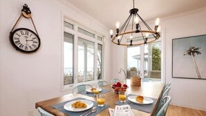 Un comedor con una mesa de madera, sillas, una araña, un reloj de pared y una ventana con vistas.
