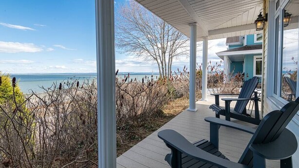 Un porche cubierto con sillas Adirondack, con vista a una playa con vegetación escasa y una vista despejada del océano.