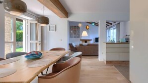 Un comedor espacioso con una mesa y sillas de madera, una cocina al fondo, y vista al exterior.