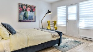 Un dormitorio con cama, una silla, una lámpara y un cuadro en la pared.