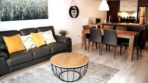 A modern living room with a black leather sofa, a round coffee table, and a dining area with a wooden table and chairs.