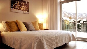 A bedroom with a large bed, a nightstand, a lamp, and a view of a snowy landscape through a window.