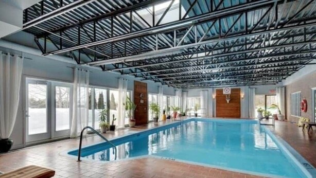 An indoor swimming pool with a high ceiling and metal beams, surrounded by windows and potted plants.