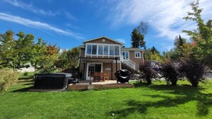 A two-story house with a covered patio, a front yard, and a large black grill.