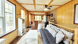 A cozy cabin interior with wooden walls, a stone accent wall, a sofa with patterned cushions, a white coffee table, and a ceiling fan.