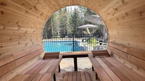 A wooden sauna with benches and a view of a swimming pool and trees. - Hôtel à la maison - Le Lys, nature et spa (Shannon)