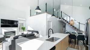 A modern kitchen with a central island, built-in dishwasher, and a dining area with a table and chairs. - Hôtel à la maison - Le Lys, nature et spa (Shannon)
