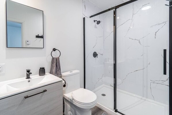 A modern bathroom with a white marble shower enclosure, a white toilet, and a sink with a towel ring.