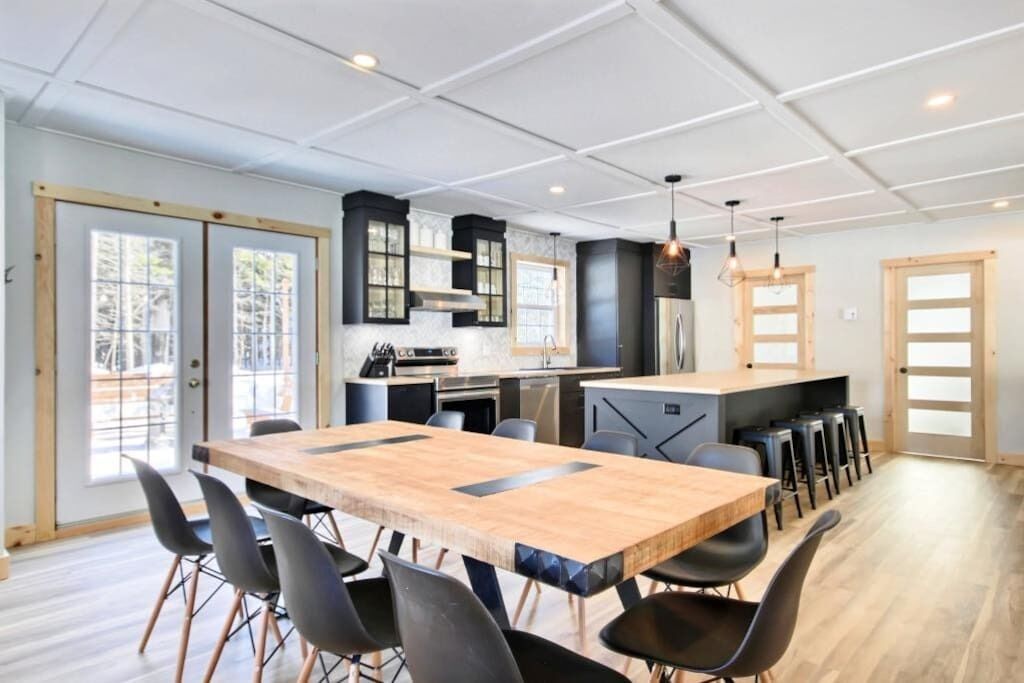 A modern kitchen with a central island, black chairs, and a wooden dining table.