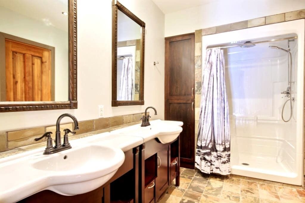 Baño con dos lavamanos, una ducha y una puerta de madera.