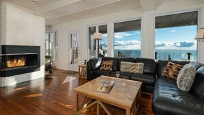 A spacious living room with a fireplace, leather sofa, and large windows offering a view of the ocean.