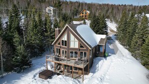Una cabaña de madera grande con un balcón, rodeada de nieve y árboles.