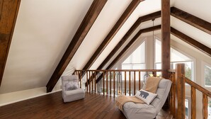 Un dormitorio tipo loft con vigas de madera, suelo de madera y dos sillones grises.