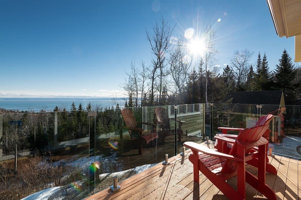 A deck with red chairs overlooking a snowy landscape and a clear view of the ocean.