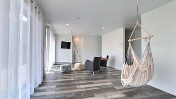 A modern living room with a wooden floor, a hanging chair, and a flat-screen TV mounted on the wall.