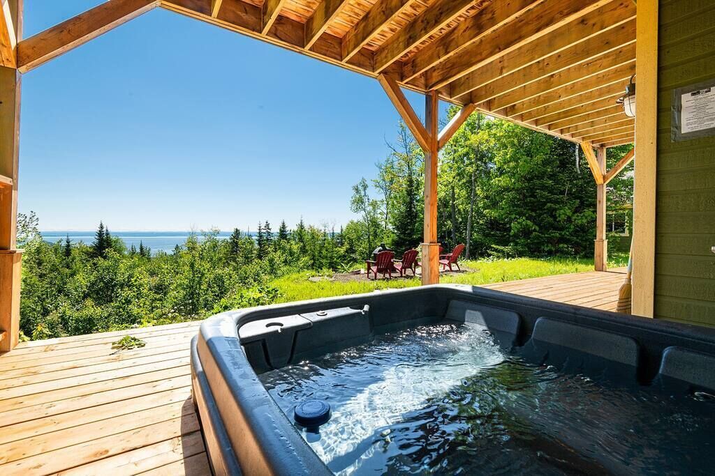 A hot tub under a wooden pergola with a view of the ocean.