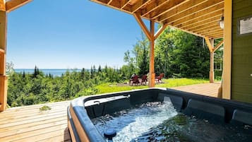 A hot tub under a wooden pergola with a view of the ocean.