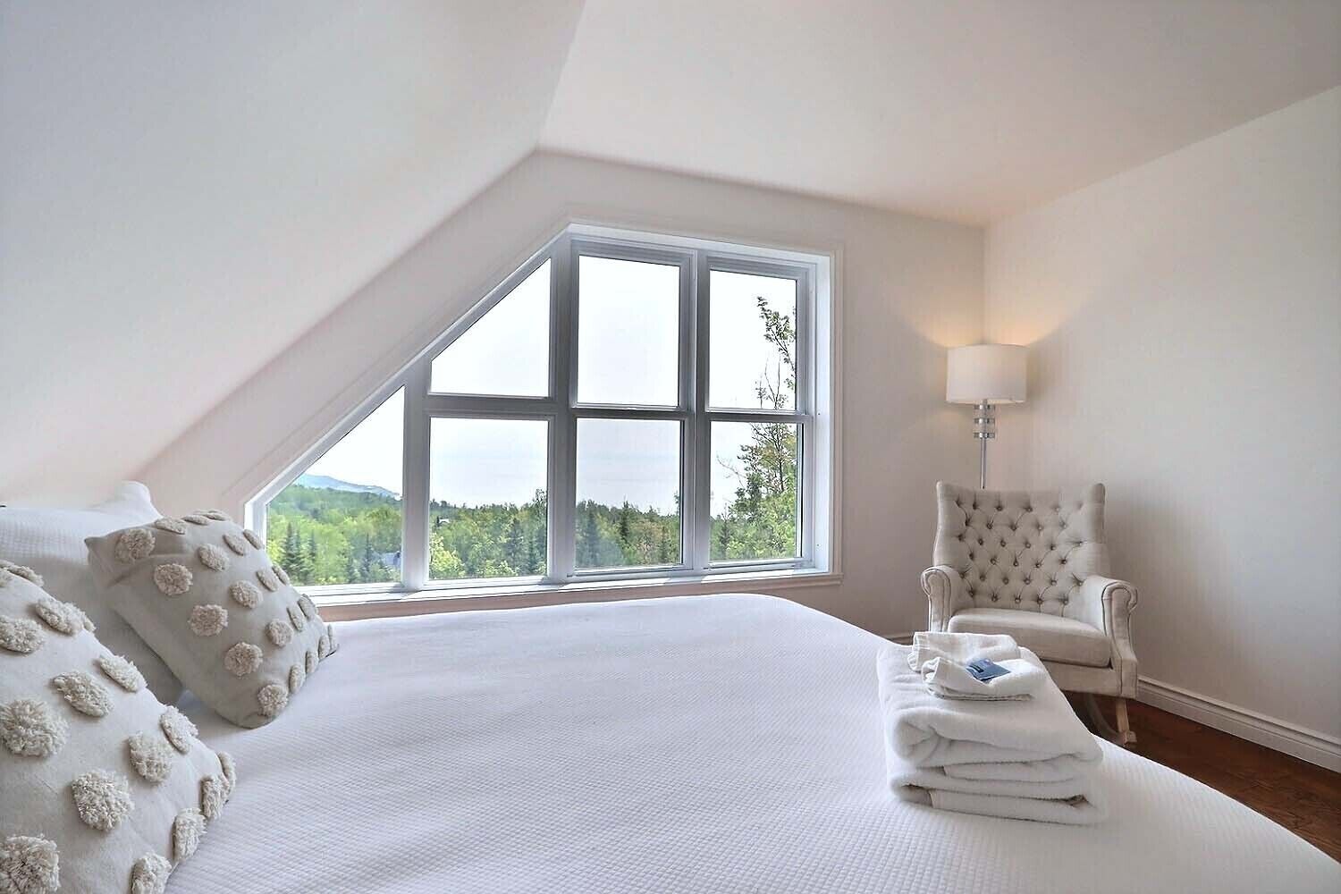 A bedroom with a large window, a bed, a chair, and a lamp.
