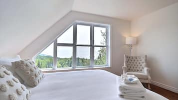 A bedroom with a large window, a bed, a chair, and a lamp.
