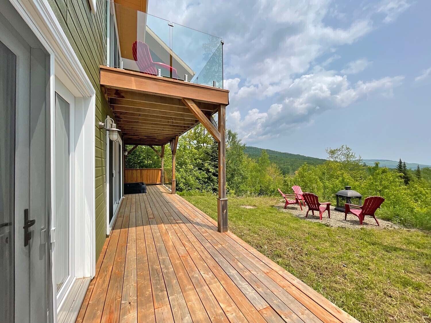 A wooden deck with a glass railing, outdoor chairs, and a gazebo.