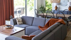 Una sala de estar moderna con un sofá seccional gris, una mesa de centro de madera y un comedor con mesa y sillas de madera.