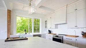 Una cocina moderna con armarios blancos, una isla grande y vista a un bosque a través de una ventana.