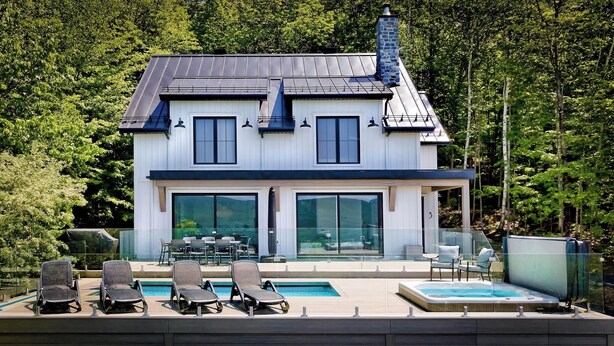 Una casa de dos plantas con un amplio ventanal, piscina y zona de estar al aire libre.