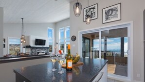 A modern kitchen with a large island, a TV mounted on the wall, and a view of the outdoors. - Hôtel à la maison - Panorama, spa et fleuve (Les Éboulements)