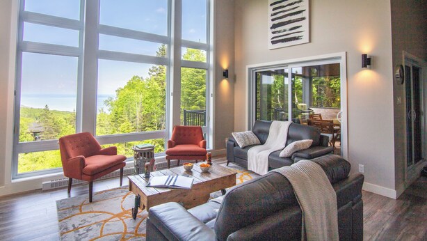A spacious living room with large windows, a fireplace, and a view of the outdoors. - Hôtel à la maison - Panorama, spa et fleuve (Les Éboulements)
