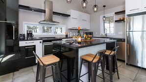 A modern kitchen with a central island, bar stools, stainless steel appliances, and pendant lighting. - Hôtel à la maison - Panorama, spa et fleuve (Les Éboulements)