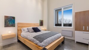 Un dormitorio moderno con una cama de madera, mesitas de noche, un ventanal grande y un armario.