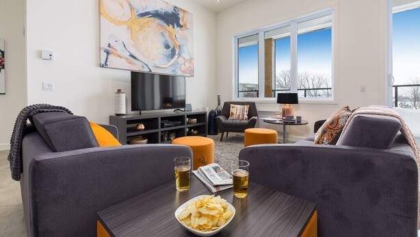 Una sala de estar moderna con un sofá gris, una mesa de centro con aperitivos y bebidas, un televisor y un cuadro abstracto grande en la pared.