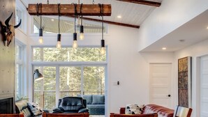 A spacious living area with a large window, a fireplace, and a dining table with chairs. - Hôtel à la maison - Chalet Kölega, spa et nature (Potton)