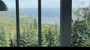 A room with a large window offering a view of a forest and a body of water.