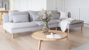 A modern living room with a grey sectional sofa, a round wooden coffee table, and a vase with flowers.