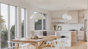 A modern kitchen with white cabinetry, a wooden dining table, and pendant lighting.