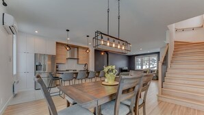 Eine moderne Küche mit Essbereich, ausgestattet mit einem Holztisch, Stühlen und Pendelleuchten.