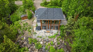A modern house with a stone patio, large windows, and a wooden deck. - Hôtel à la maison - Le Phare d'Irène spa et fleuve (Saint-Irénée)