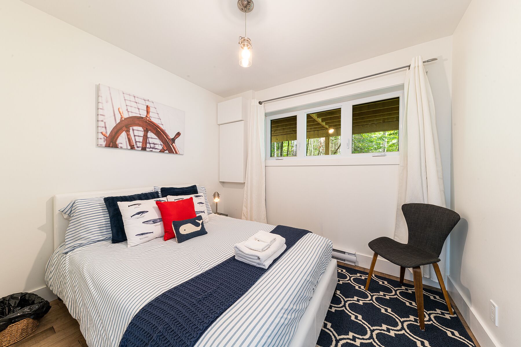 A bedroom with a bed, a chair, a window, and a wall-mounted artwork.