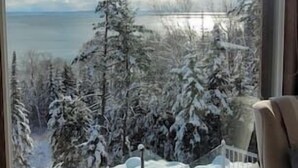 A room with a large window offering a view of a snowy landscape with trees and a body of water. - Hôtel à la maison - Le Phare d'Irène spa et fleuve (Saint-Irénée)