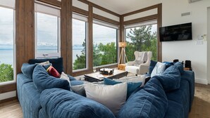 A modern living room with large windows, a sofa, a coffee table, and a TV. - Hôtel à la maison - Le Phare d'Irène spa et fleuve (Saint-Irénée)