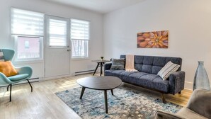 A modern living room with a sofa, armchair, coffee table, and a painting on the wall. - Hôtel à la maison - Le Gaillard (Montreal)
