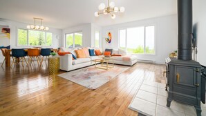 Een ruime woonkamer met een groot raam, een open haard en een eethoek met stoelen en een tafel.