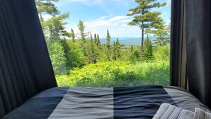 Una cama con vista a un bosque y montañas a través de una ventana.