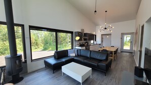 Un salón moderno con un sofá de cuero negro, una mesa de centro blanca y un ventanal con vistas a árboles.