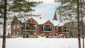Un chalet à plusieurs étages, dont le sol est recouvert de neige, et qui est entouré d’arbres.