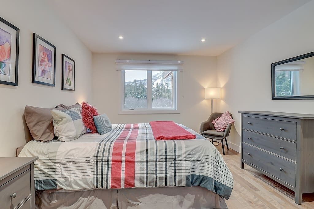 Une chambre à coucher avec un lit, une commode, une chaise et une fenêtre donnant sur des arbres.