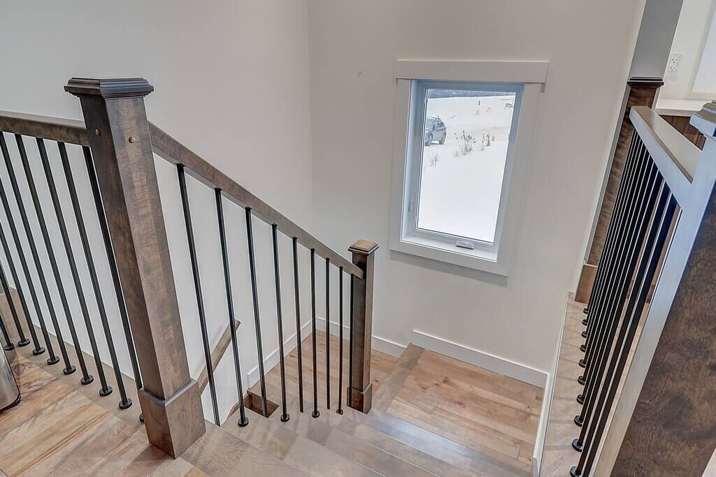 A modern staircase with a wooden handrail and metal balusters, leading to a room with a large window offering a view of the outdoors.