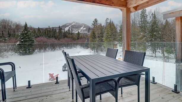 Un espace extérieur abrité, doté d’une table et de chaises, qui offre une vue sur un paysage enneigé et une montagne.