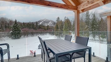 Un espace extérieur abrité, doté d’une table et de chaises, qui offre une vue sur un paysage enneigé et une montagne.